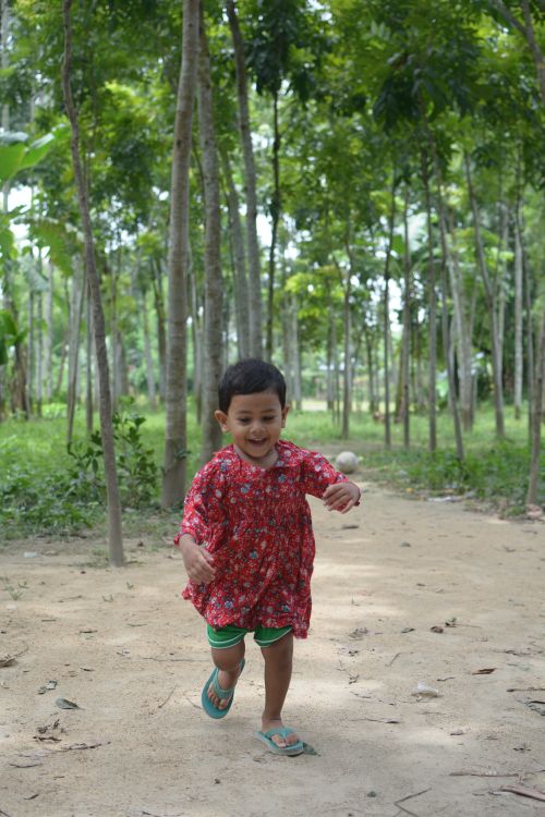 Free A cheerful child in a red outfit joyfully running through a vibrant, green forest pathway. Stock Photo