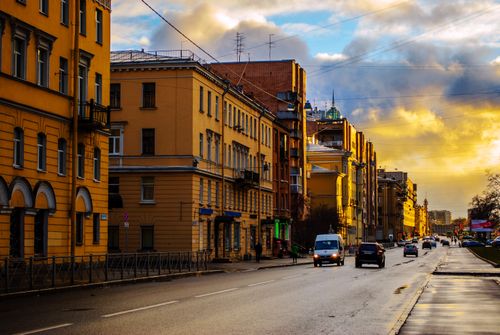 Free Scenic view of a city street lined with historic buildings during sunset, featuring cars and a vibrant sky. Stock Photo