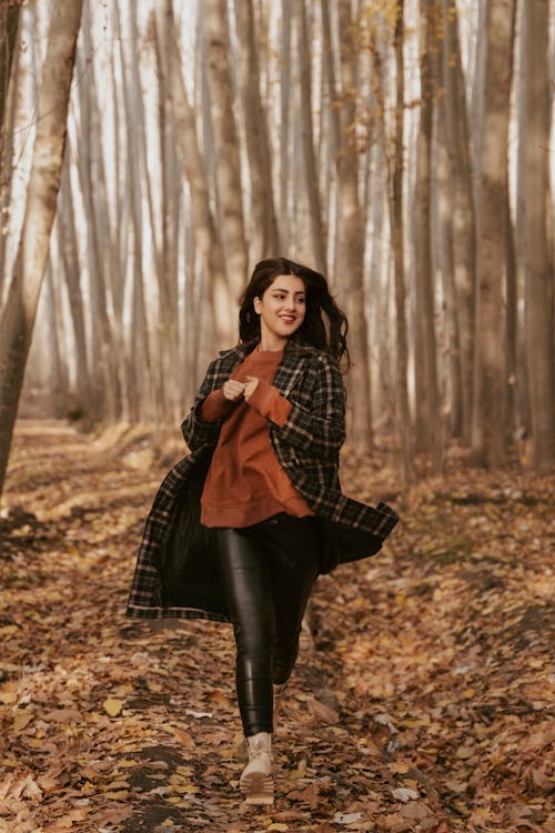 Woman in Black and Red Plaid Dress Running on Brown Dried Leaves