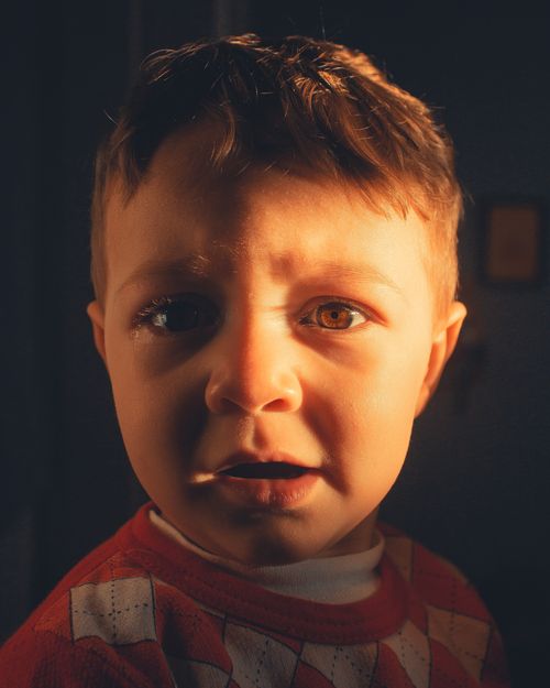 Free Close-up portrait of a young boy in warm lighting, capturing an emotional expression. Stock Photo