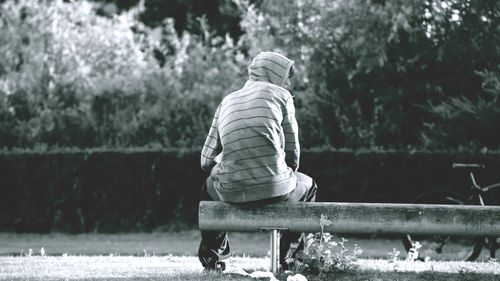Free Man in hoodie sitting alone on a park bench in monochrome setting. Stock Photo