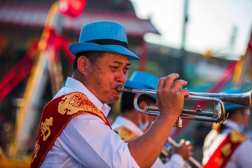 Free A male musician in Taiwan plays trumpet at an outdoor festival, wearing a blue hat and traditional attire. Stock Photo