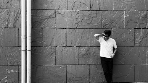 Free Black and white image of a man leaning against a textured stone wall, exuding a minimalist and modern vibe. Stock Photo