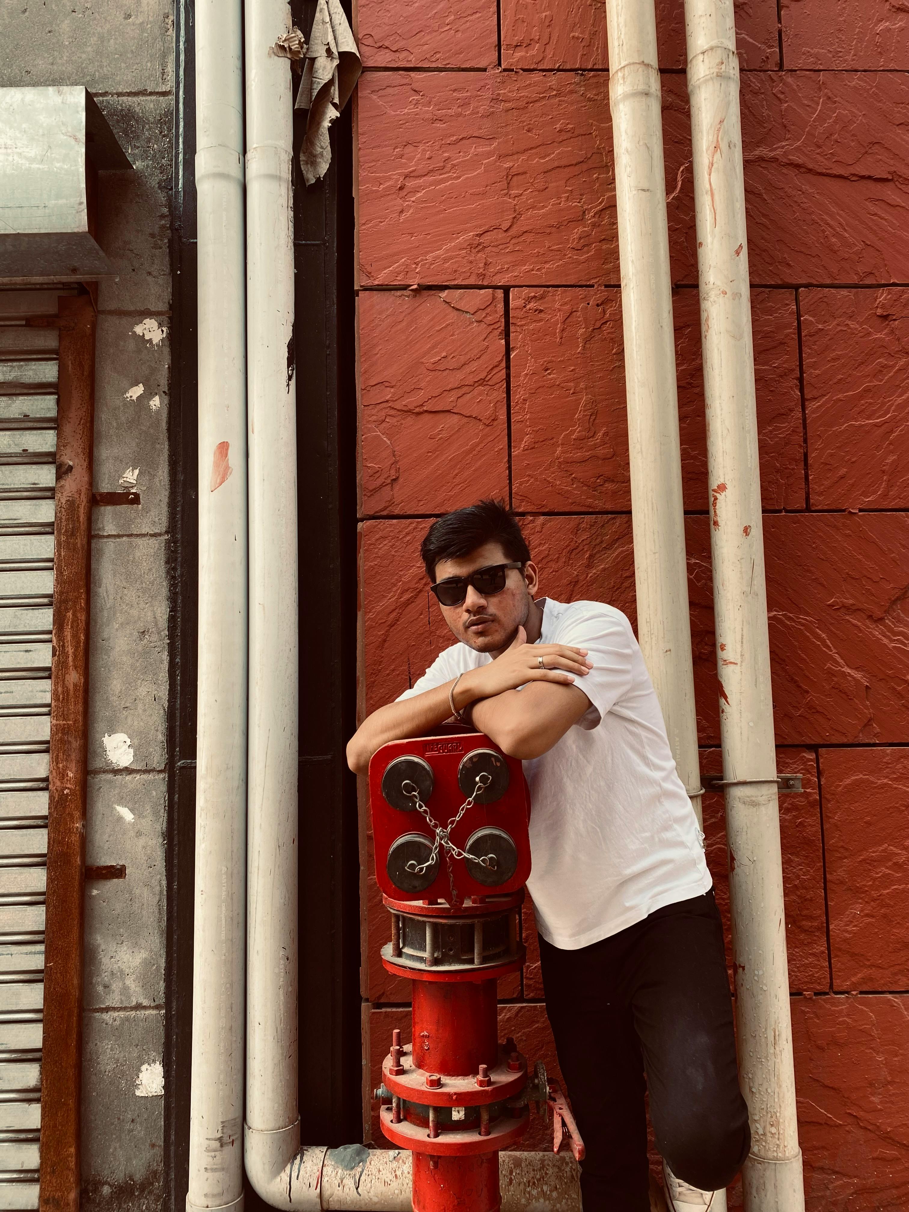 Casual urban portrait of a young man leaning on a red hydrant against a textured wall.