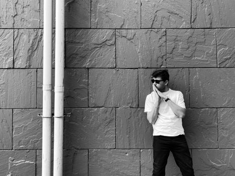 Black and white portrait of a man leaning against a textured stone wall, exuding style.