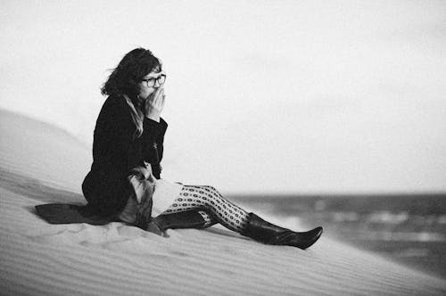 Grayscale Photo of Woman Sitting on Sand