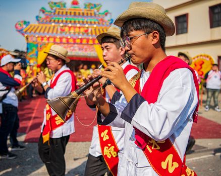 Men playing traditional wind instruments at a Taiwanese festival parade outdoors.