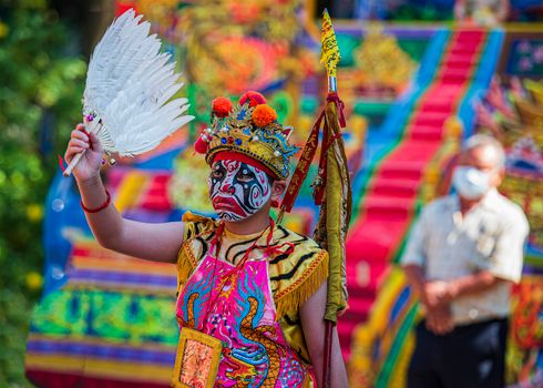 A colorful performer in traditional attire and face paint during a vibrant ceremony in Taiwan.