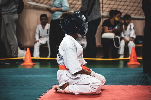 Free Boy in protective gear practices martial arts in indoor dojo setting surrounded by others. Stock Photo