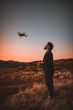 A man controls a drone during a picturesque sunset in a grassy landscape.