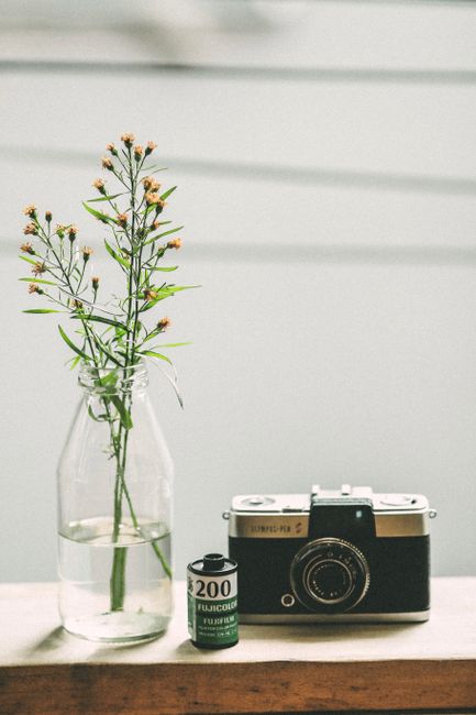 Elegant vintage camera and film roll beside a delicate floral arrangement in a glass vase.