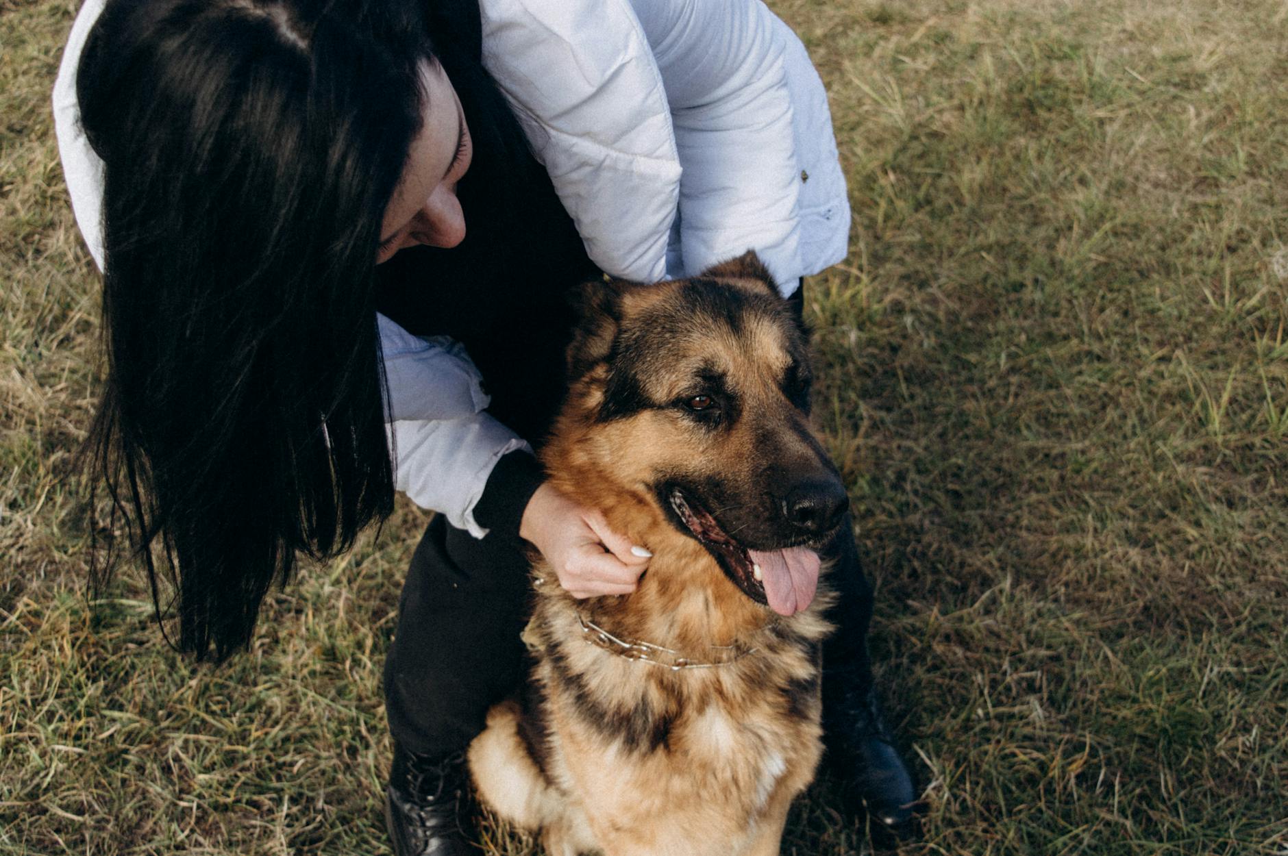 A woman lovingly petting a German Shepherd dog in a grassy outdoor setting.