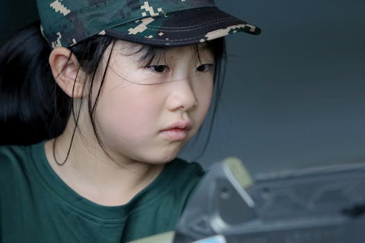 A young girl intensely focused, wearing a camouflage cap and green shirt indoors.