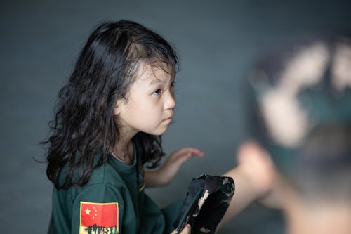 A Young Girl in Blue Crew Neck Shirt Holding a Army Cap