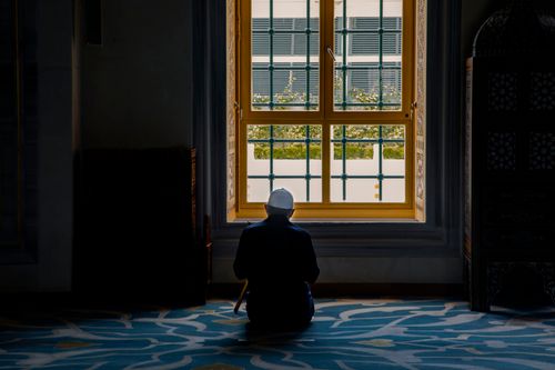 Free Person in silhouette kneeling in a peaceful interior space by a large window, exuding tranquility and contemplation. Stock Photo