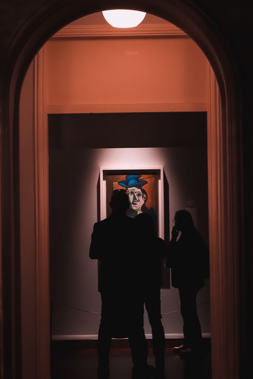 Silhouettes of visitors looking at colorful abstract art in a gallery corridor.