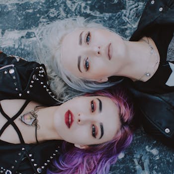 Stylish portrait featuring two women with striking hair colors and edgy fashion in an artistic pose.