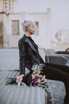 一位穿着皮夹克的别致女人坐在屋顶上，手捧鲜花，散发着都市风格