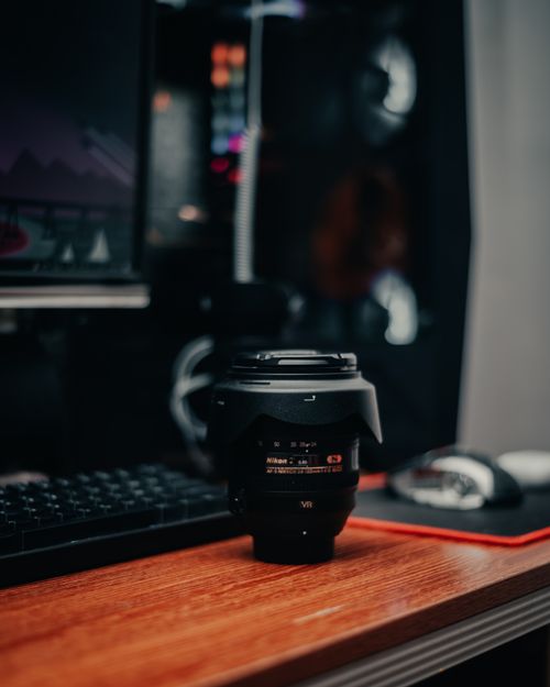 Free A camera lens on a desk beside computer accessories in a moody setup. Stock Photo
