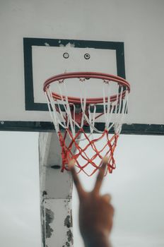A unique perspective of a basketball hoop and backboard with a hand showing a peace sign.