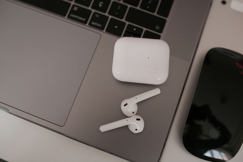 White wireless earbuds beside their case resting on a laptop