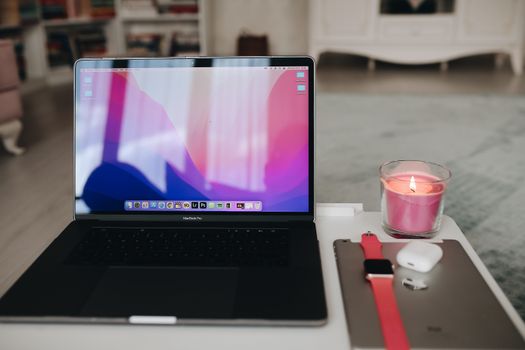 A modern workspace setup featuring a laptop, candle, AirPods, and Apple Watch.