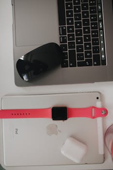Overhead view of a workspace featuring a laptop, tablet, smartwatch, and wireless earbuds.
