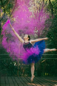 Ballet dancer performing with colorful smoke on a wooden stage outdoors.