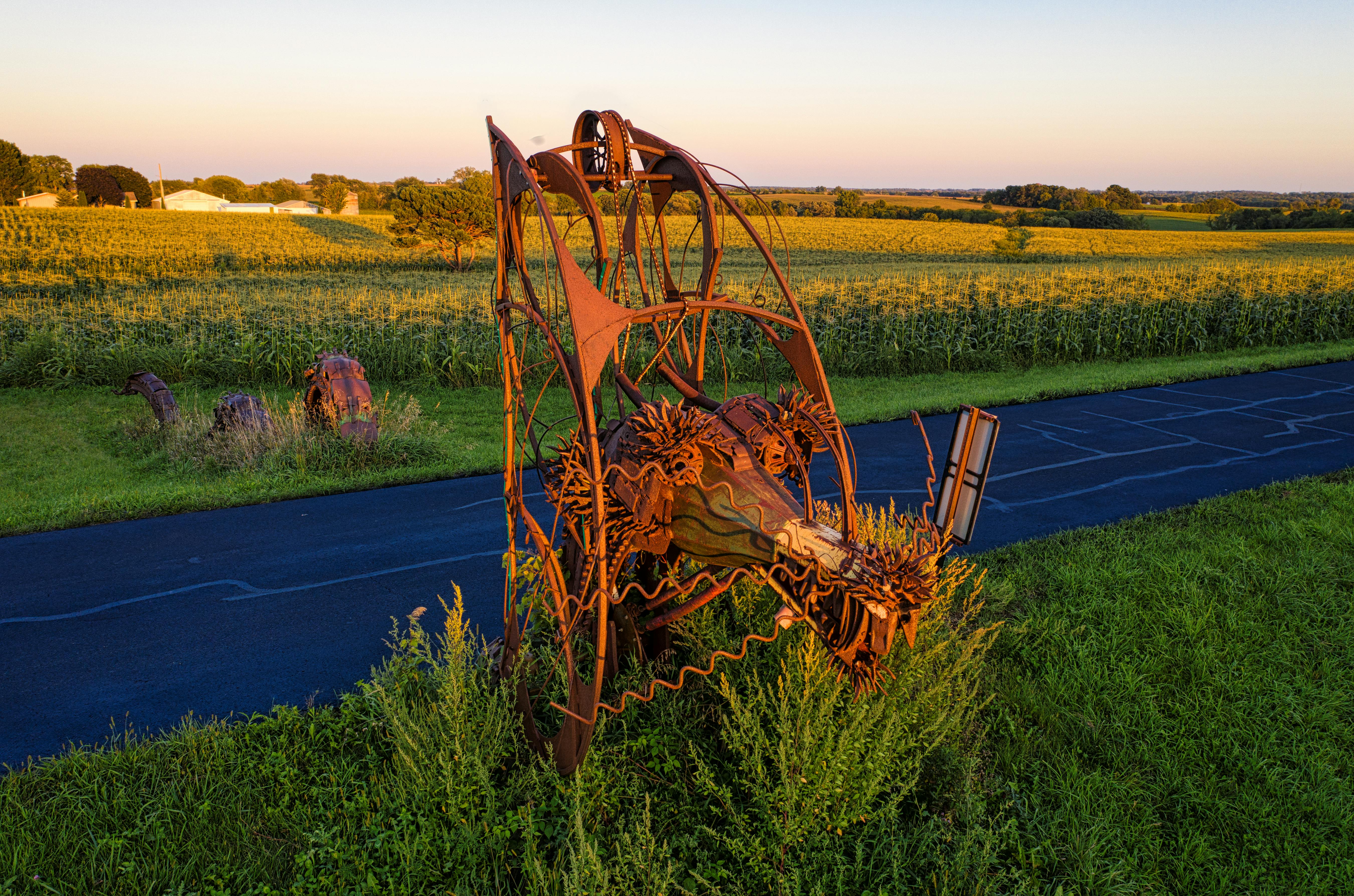 Rusty metal sculpture in a rural Minnesota field during sunset, showcasing agricultural beauty.