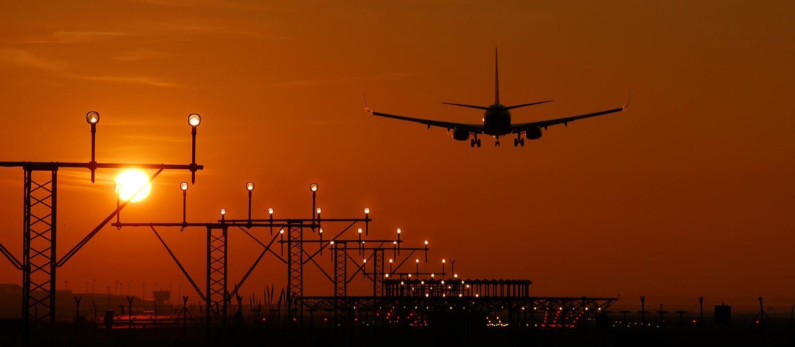 Silhouette of an airplane landing during sunset at Barcelona airport, with a vibrant orange sky.