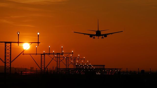 Silhouette of an airplane landing during sunset at Barcelona airport, with a vibrant orange sky. — lounges at Barcelona Airport