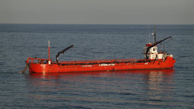 A vibrant red cargo ship sailing in the calm Mediterranean waters near Montgat, Spain.