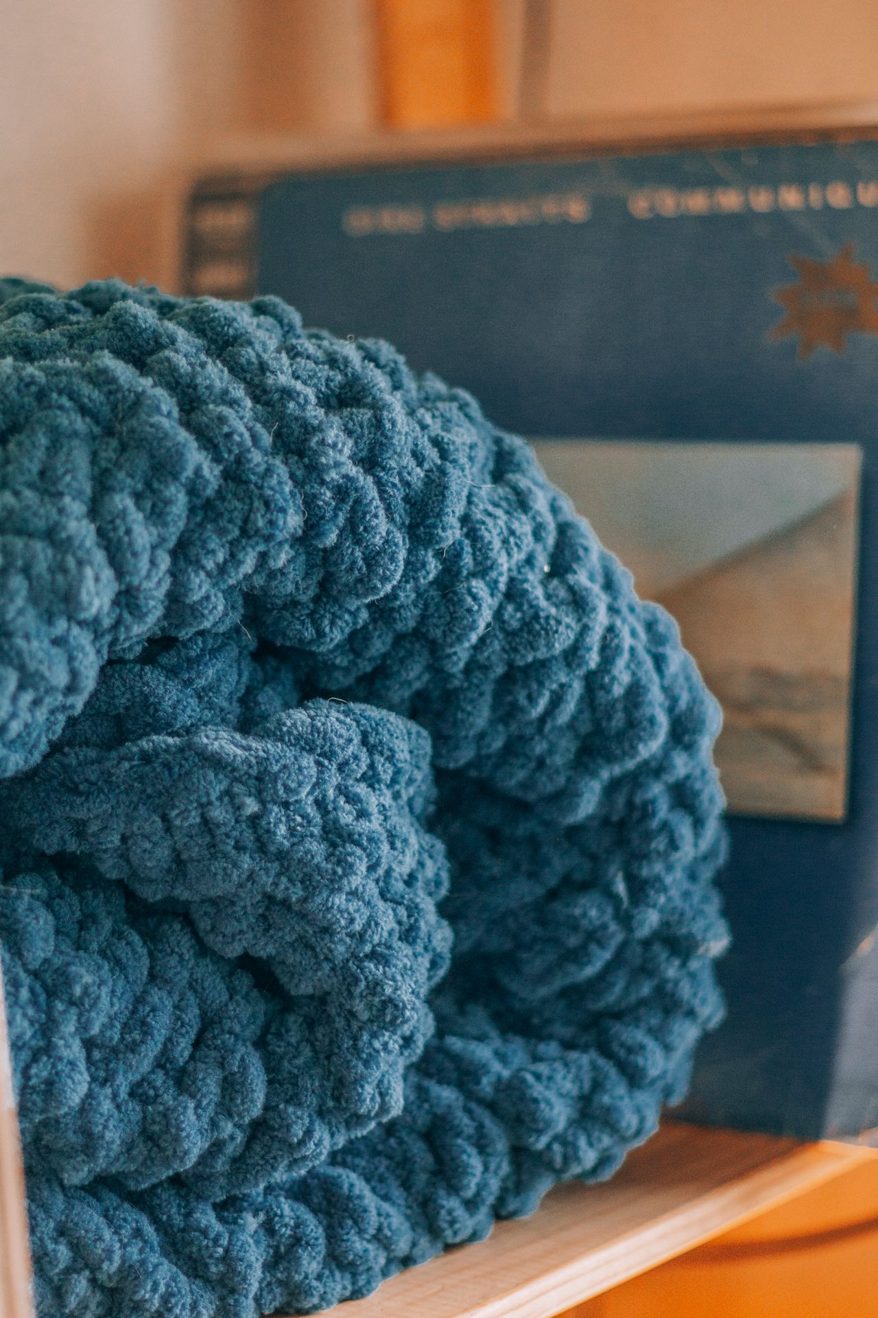 Folded blue chunky-knit blanket on a wooden shelf with a book behind it