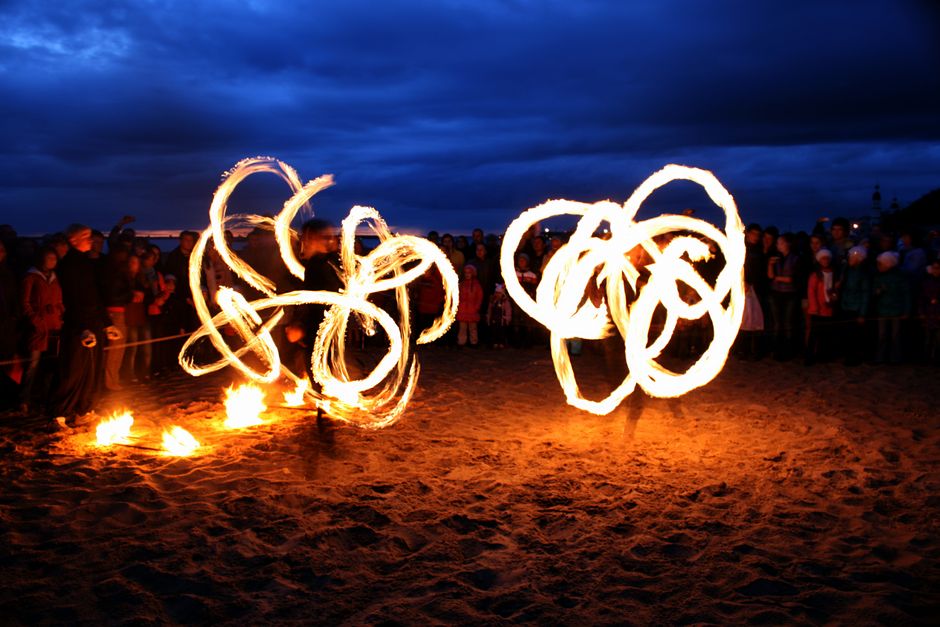 Striking long exposure photo of fire dancing on a sandy beach at night with a captivated audience.