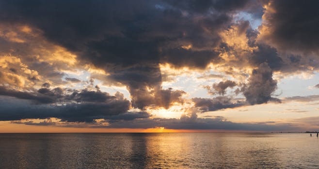 A breathtaking sunset with dramatic clouds reflecting on the tranquil ocean surface.