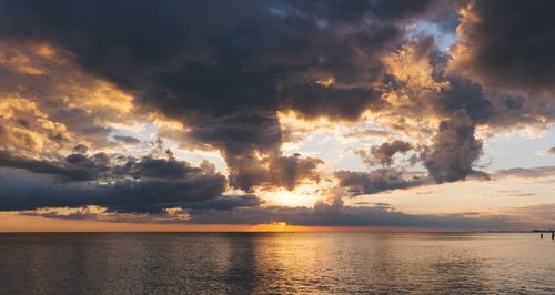 Free A breathtaking sunset with dramatic clouds reflecting on the tranquil ocean surface. Stock Photo