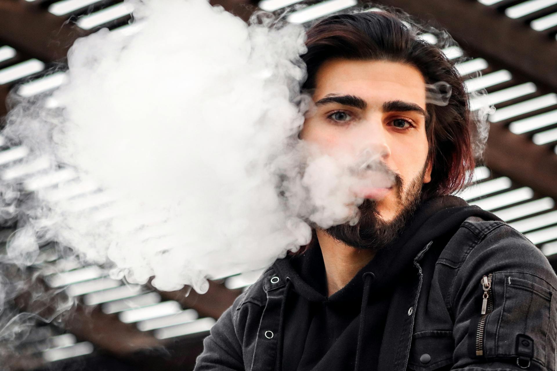 Man with a beard vaping outdoors, releasing smoke clouds in Dubai.