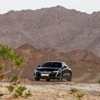 A luxury sedan car driving on a dirt road amidst rocky desert mountains in Dubai.