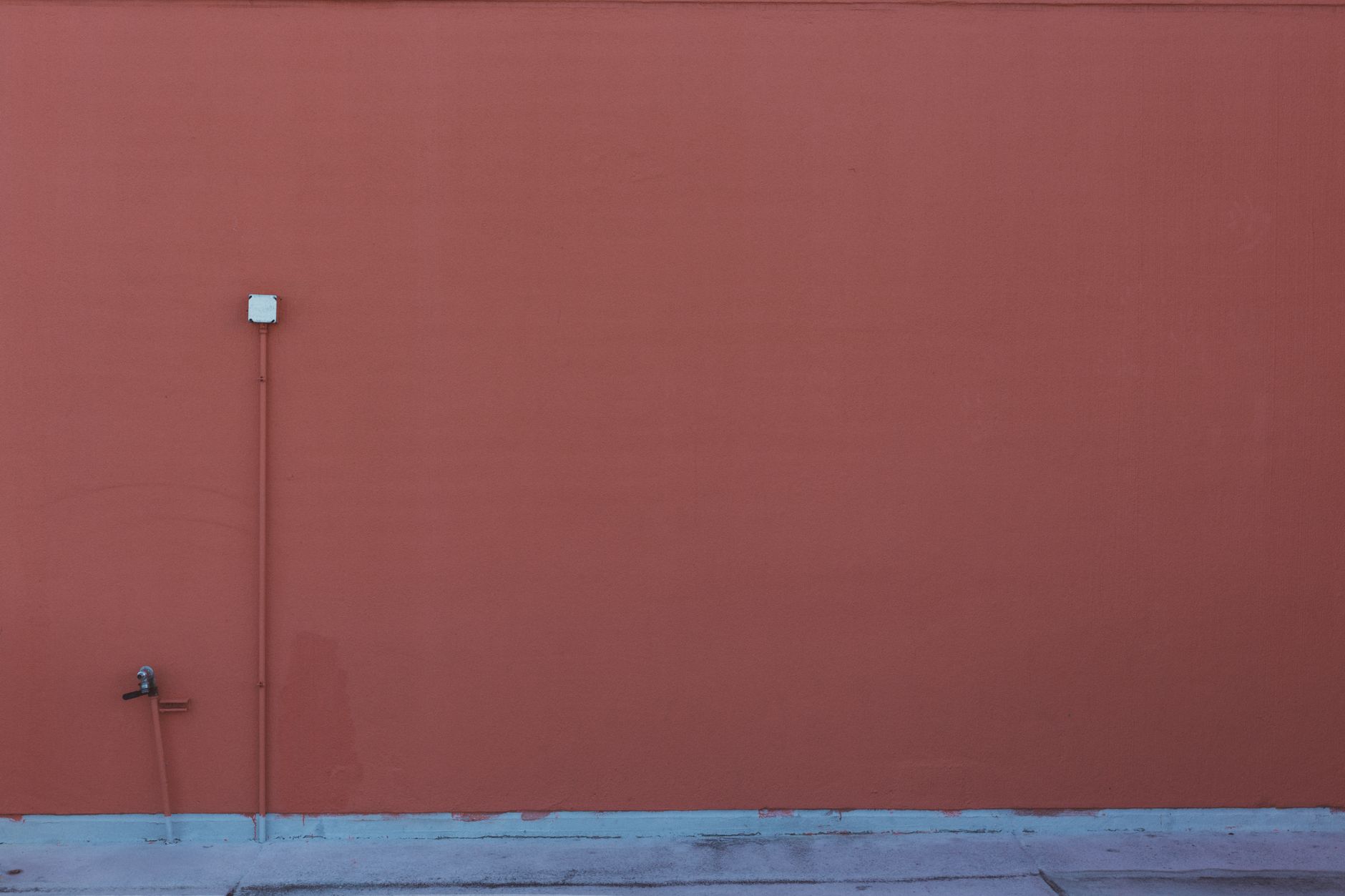 An orange-painted wall featuring a pipe and electrical outlet, perfect for minimalism themes.