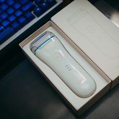 White cordless foil shaver with a blue trim ring lying in its opened cream box beside a backlit keyboard