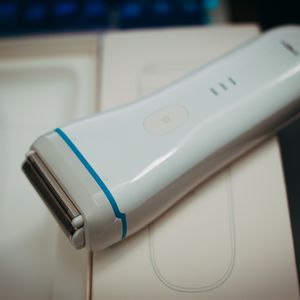 White cordless lady shaver with a foil head and a blue trim ring resting on its opened cream box