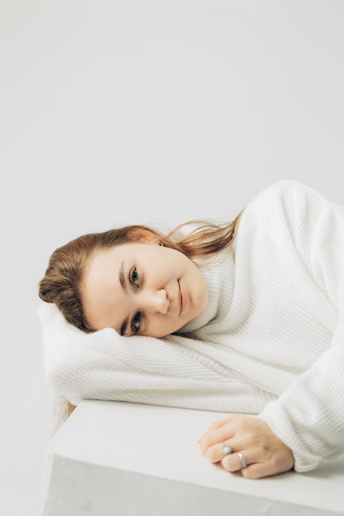 Woman in White Sweater Lying on White Surface