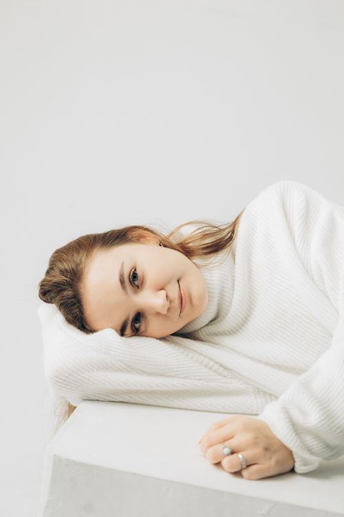 Free Young woman in a white sweater resting indoors, showcasing serene beauty. Stock Photo