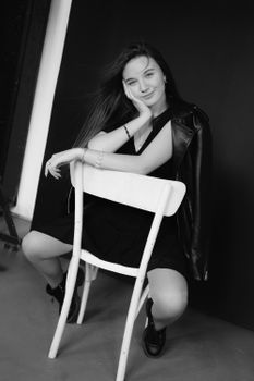Elegant black and white portrait of a woman sitting on a chair in a studio.