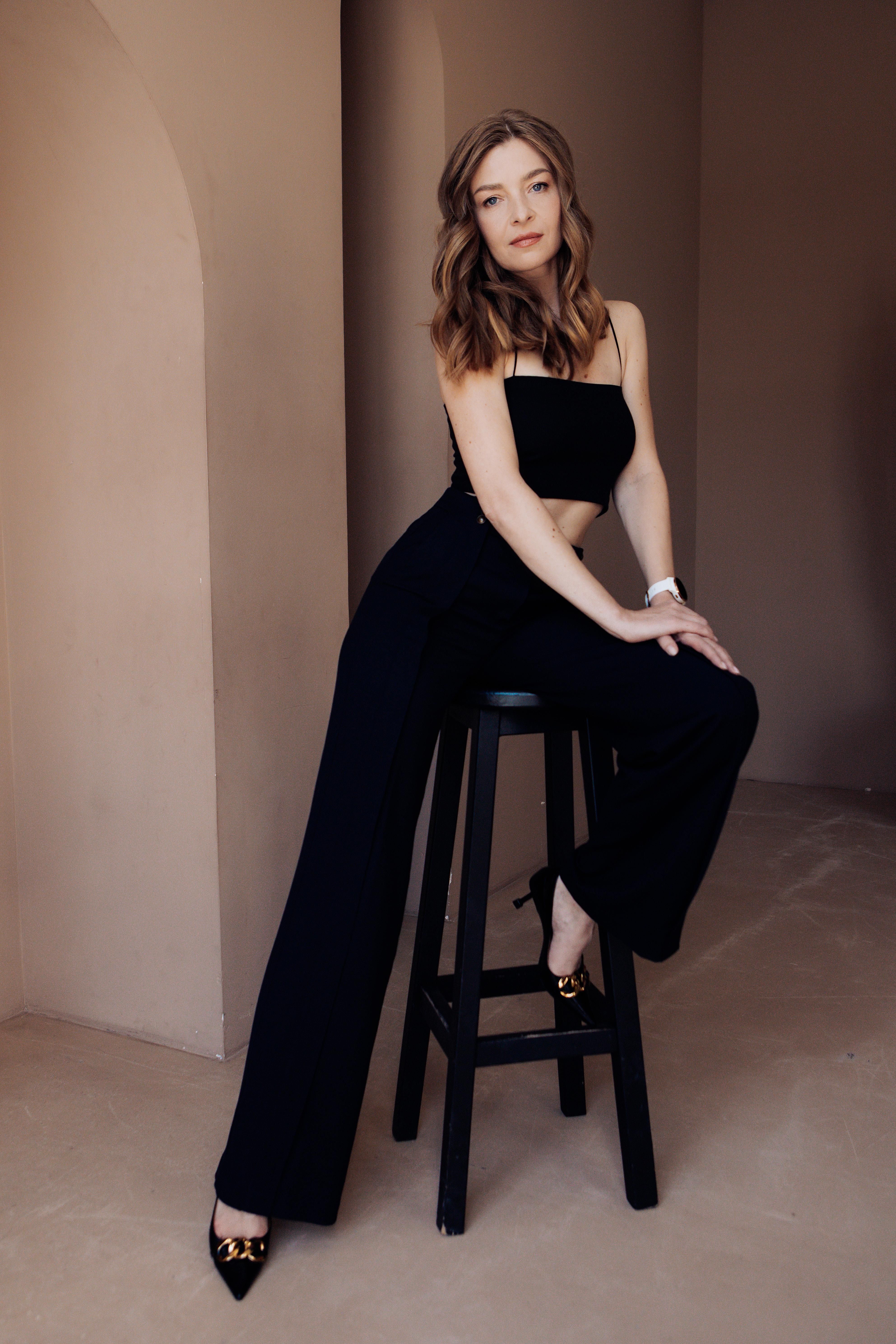 Stylish woman with wavy hair sitting elegantly on a bar stool in a modern setting.