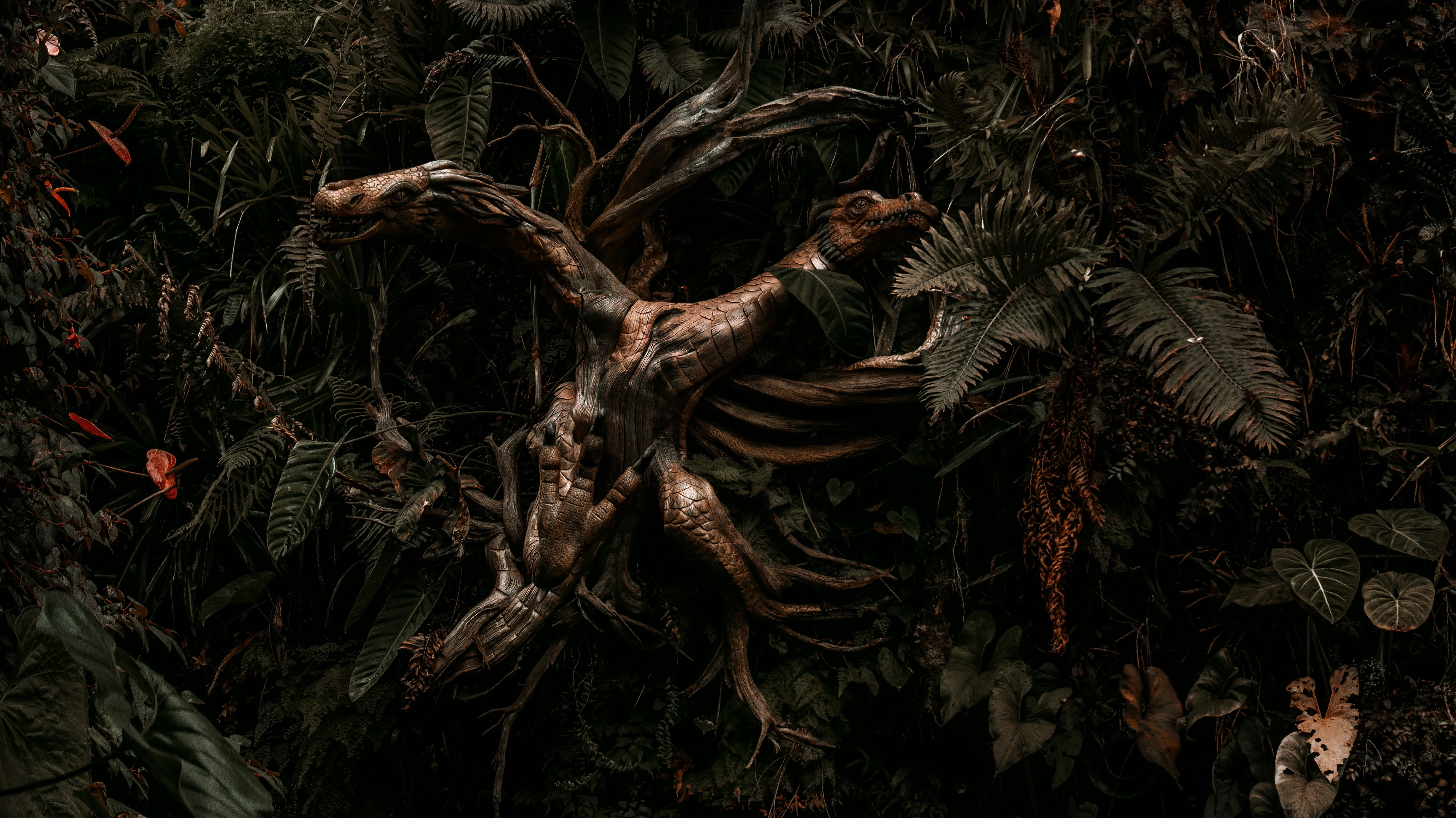 An intricate wooden dragon sculpture surrounded by dense, lush jungle plants and ferns.