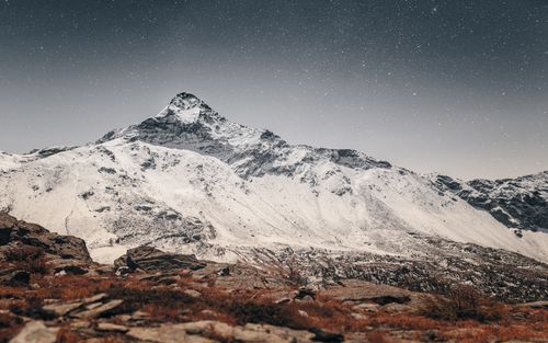 Free A breathtaking view of a snow-covered mountain peak under a clear starry night sky in winter. Stock Photo