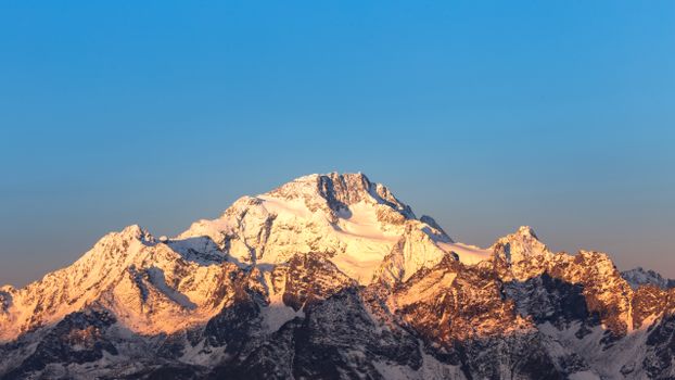 Breathtaking view of snow-covered peaks in the Italian Alps against a clear blue sky during sunrise.