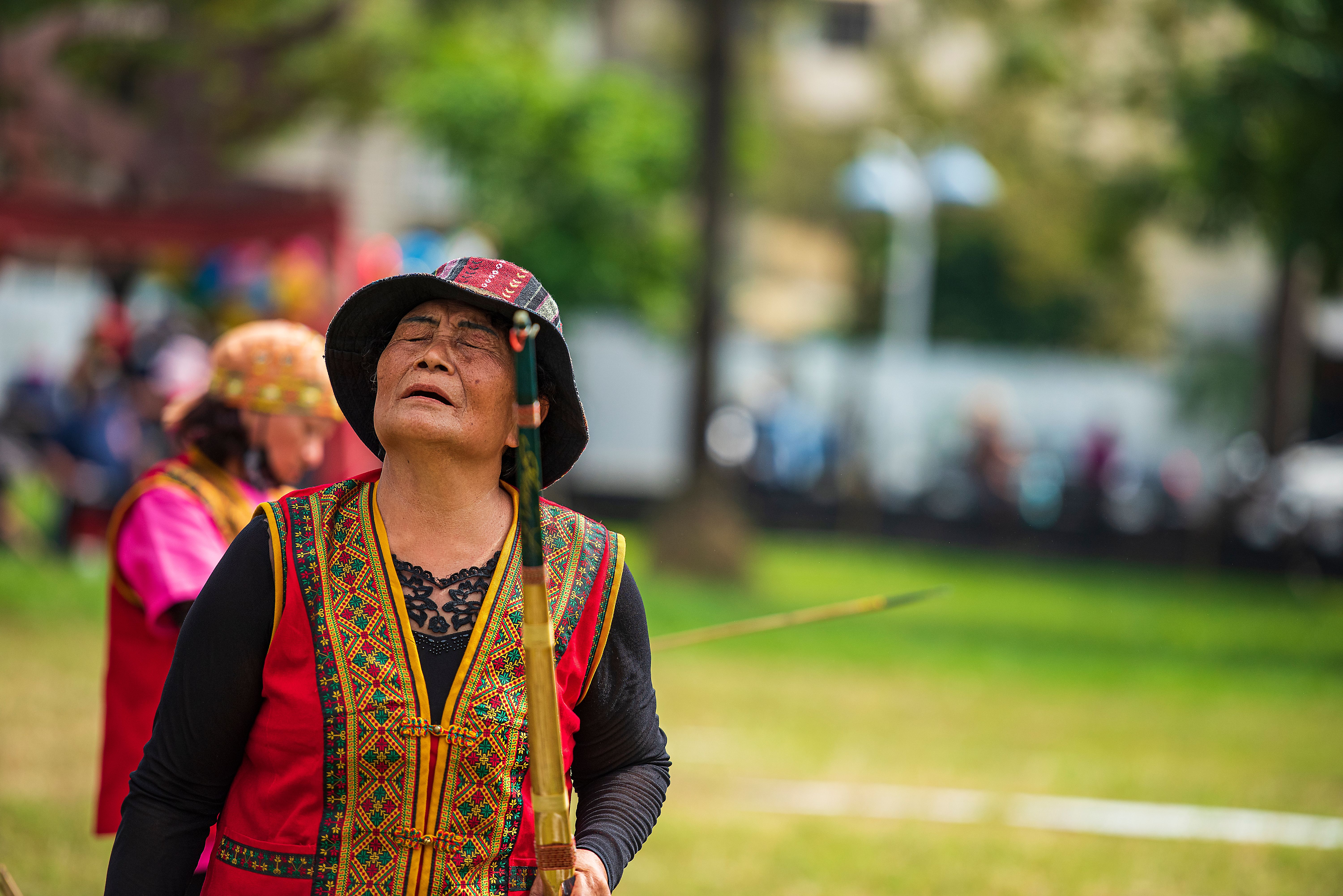 An elderly Taiwanese woman in vibrant traditional attire participates in an outdoor cultural event.