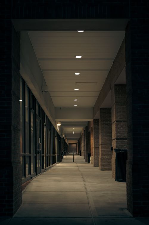 Free Empty indoor hallway with glass panels and overhead lights, offering a modern architectural look. Stock Photo